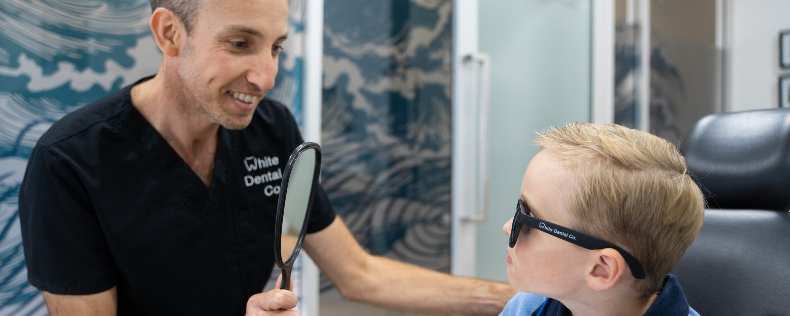 Dr Nick White holds a mirror so a young child can check their smile after an appointment