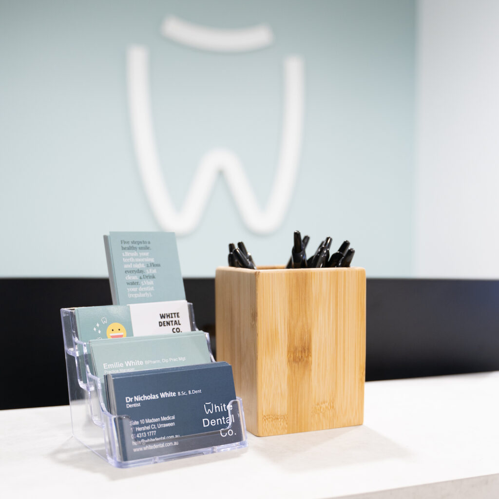 Detail of White Dental Co.’s reception desk with business cards and brochures about dental health. The White Dental Co. logo adorns the wall behind the desk.