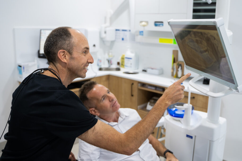 Dr Nick points to a detail in a dental x-ray while the patient looks on