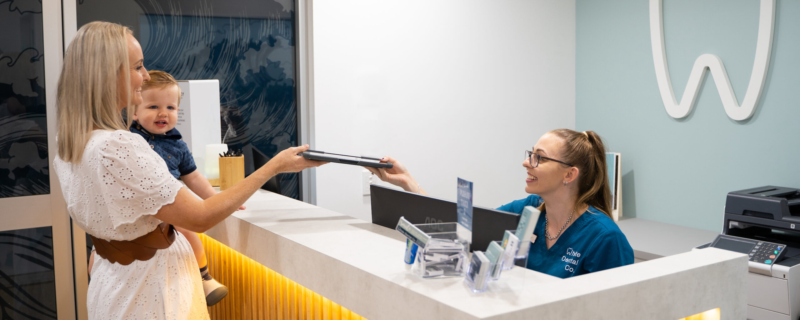 A mother holding an infant chats to Lucy as she completes her child’s pre-appointment paperwork