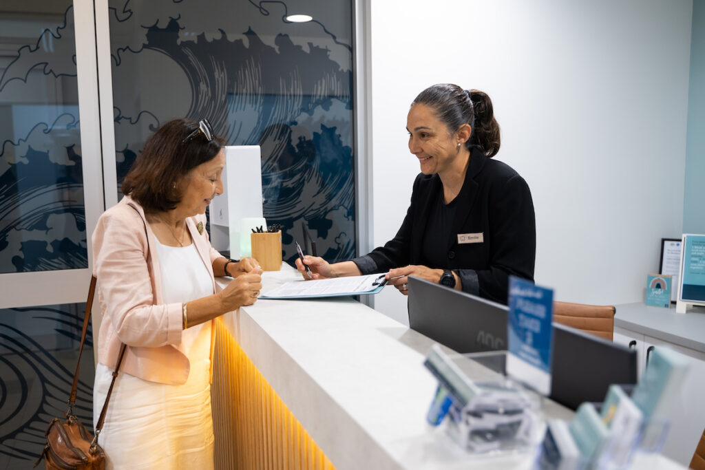 Practice manager, Emilie White, chats with a patient as she completes paperwork at the reception desk