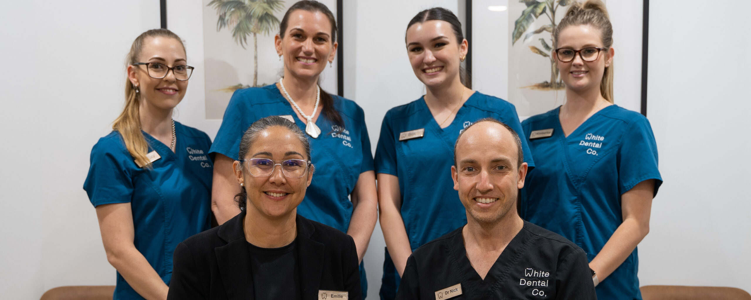 Practice manager Emilie White and principal dentist Dr Nick White, both dressed in black, sit in front of the rest of the clinical team, who are wearing mid-blue uniforms.