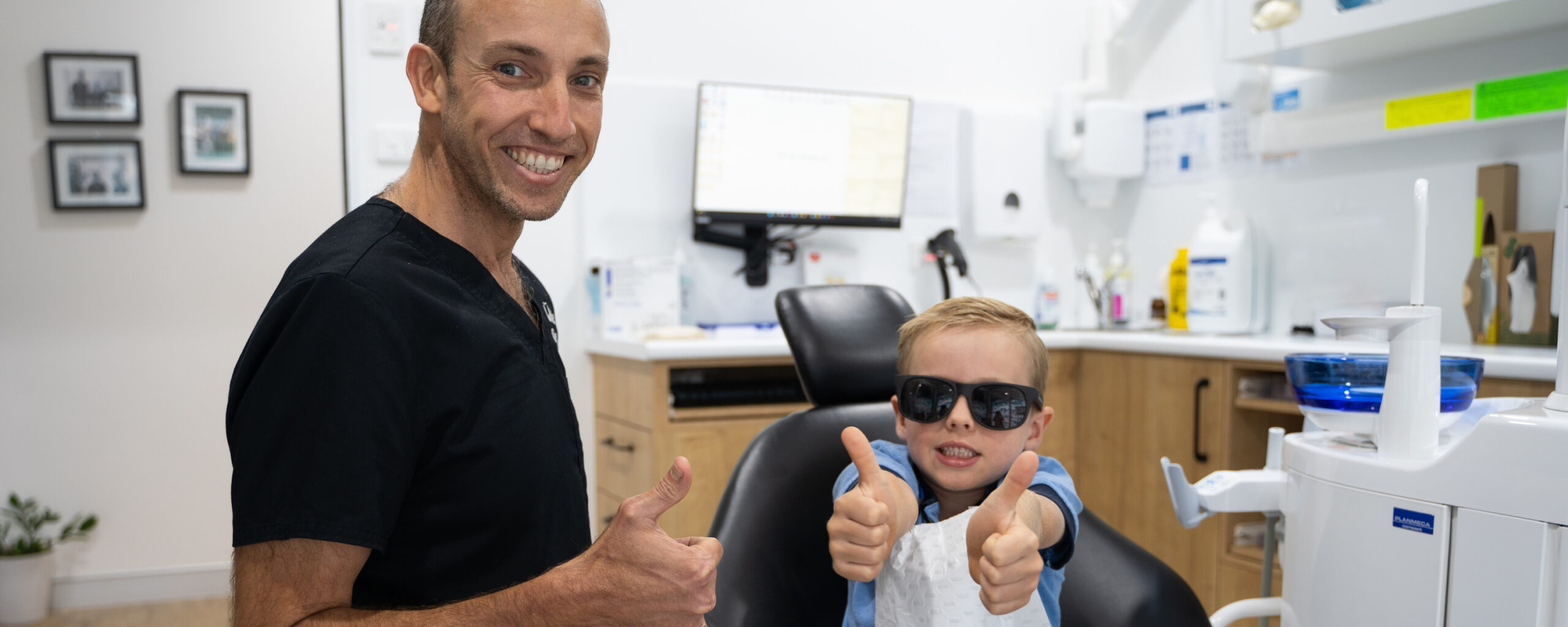 Dr Nick White and a young patient smile with their thumbs up at the end of a fissure sealant appointment