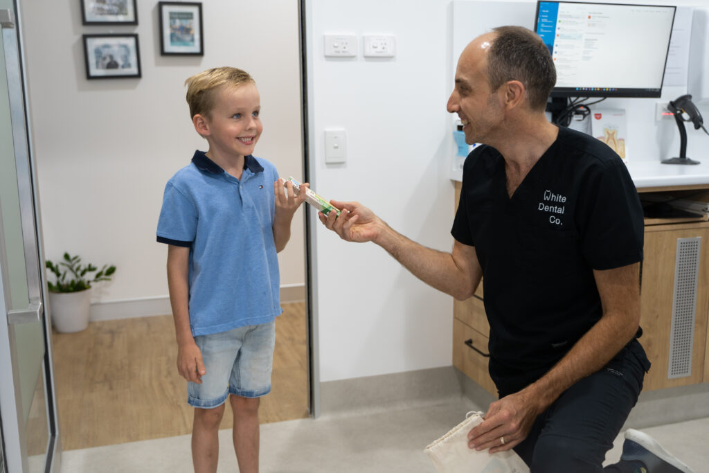 A young child smiles as Dr Nick hands him a toothbrush following a dental appointment