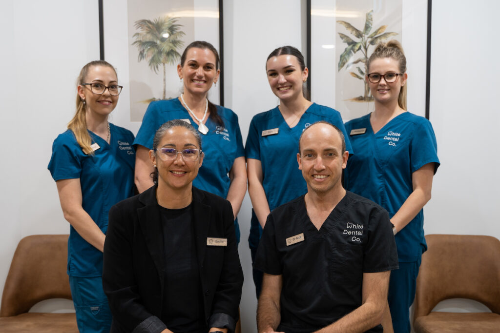 Dentist Dr Nick White and practice manager Emilie White sit for a portrait with their clinical team standing behind them.