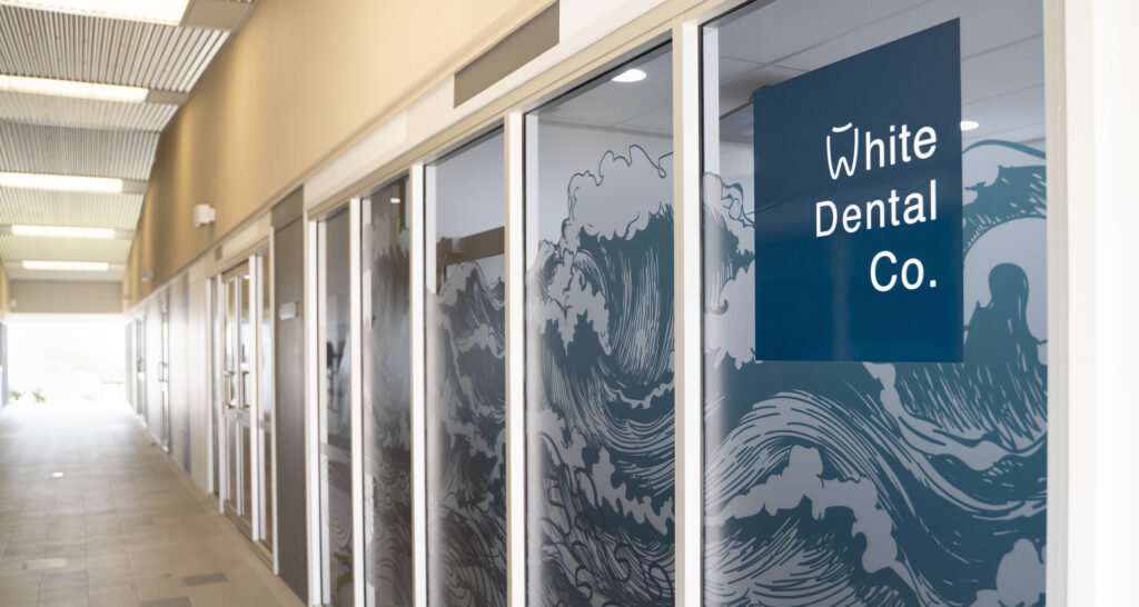 The front doors of White Dental Co. as seen through the breezeway of the Madsen Medical Centre. They are decorated with large blue and white waves.